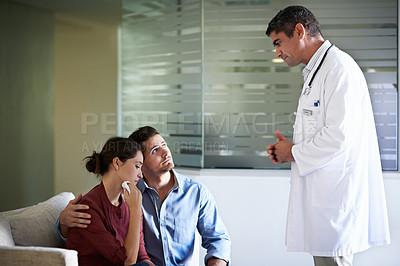 Buy stock photo Shot of a doctor talking to a grieving woman and her husband in a hospital waiting room