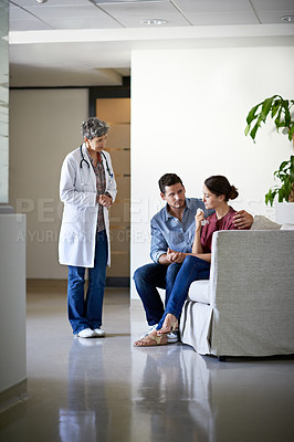 Buy stock photo Shot of a doctor talking to a husband comforting his wife in a hospital waiting room