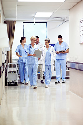 Buy stock photo Shot of a team of doctors walking and talking in a hospital corridor