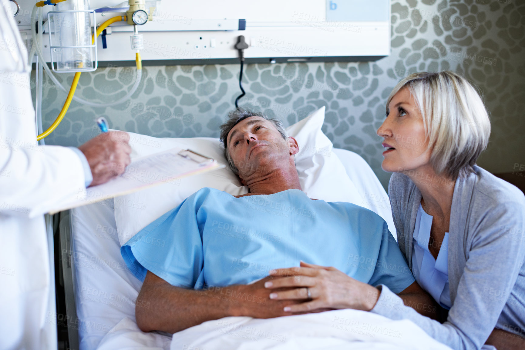 Buy stock photo Shot of a wife visiting her husband in the hospital while a doctor looks on