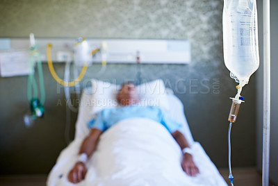 Buy stock photo Closeup shot of an IV drip with an unconscious patient in the background