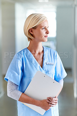 Buy stock photo Shot of a thoughtful-looking nurse standing in a hospital corridor