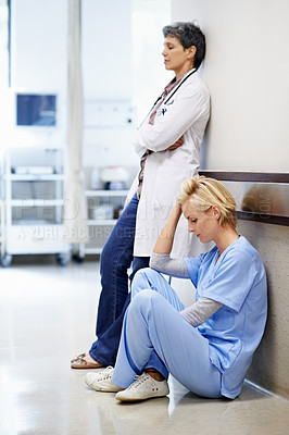 Buy stock photo Shot of two tired looking doctors in a hospital corridor