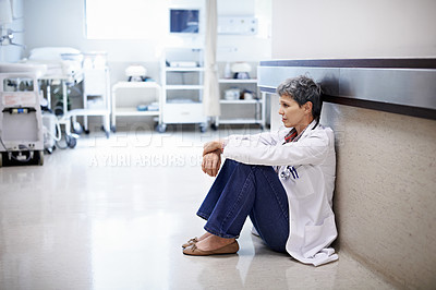 Buy stock photo Shot of an exhausted doctor sitting in a hospital corridor