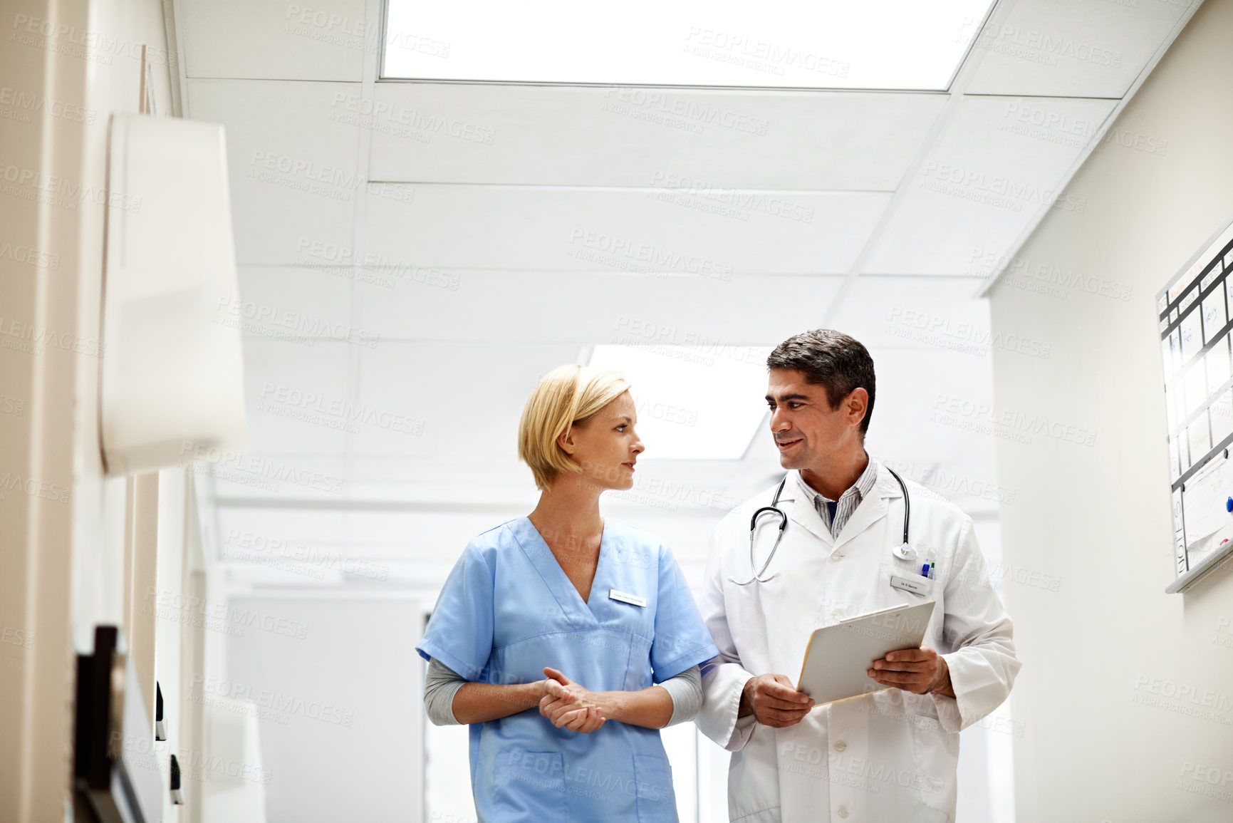 Buy stock photo Shot of two doctors talking while walking down a hospital corrider