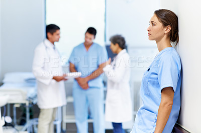 Buy stock photo Shot of a tired looking nurse leaning against a wall with colleagues in the background