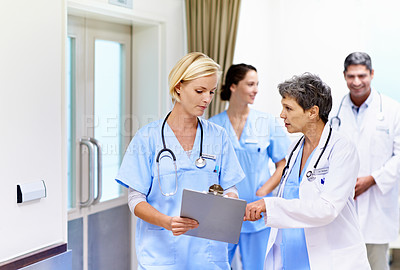Buy stock photo Shot of a team of doctors walking and talking in a hospital corridor