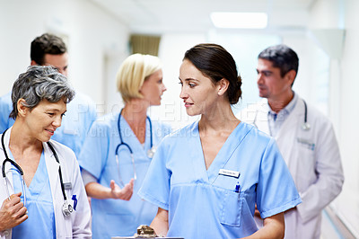 Buy stock photo Shot of a team of doctors walking and talking in a hospital corridor