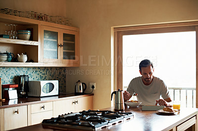 Buy stock photo Shot of a man using his digital tablet while eating breakfast at home
