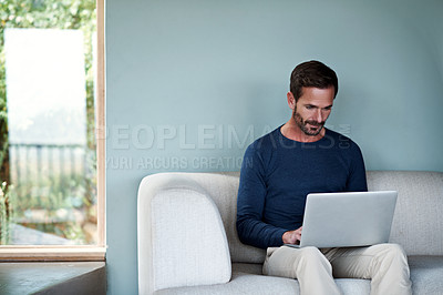 Buy stock photo Shot of a man using a laptop on his living room sofa