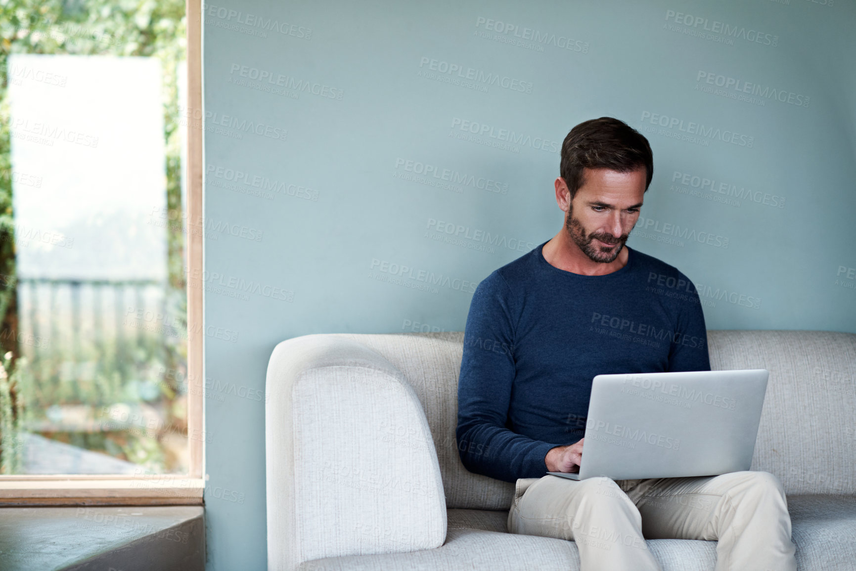Buy stock photo Shot of a man using a laptop on his living room sofa