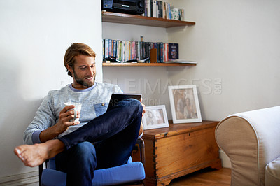 Buy stock photo Shot of a young man using a digital tablet while relaxing at home