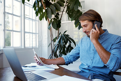 Buy stock photo Shot of a young man talking on the phone while looking at paperwork