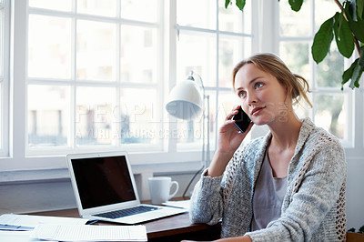 Buy stock photo Shot of a young woman talking on the phone while working on a laptop at home