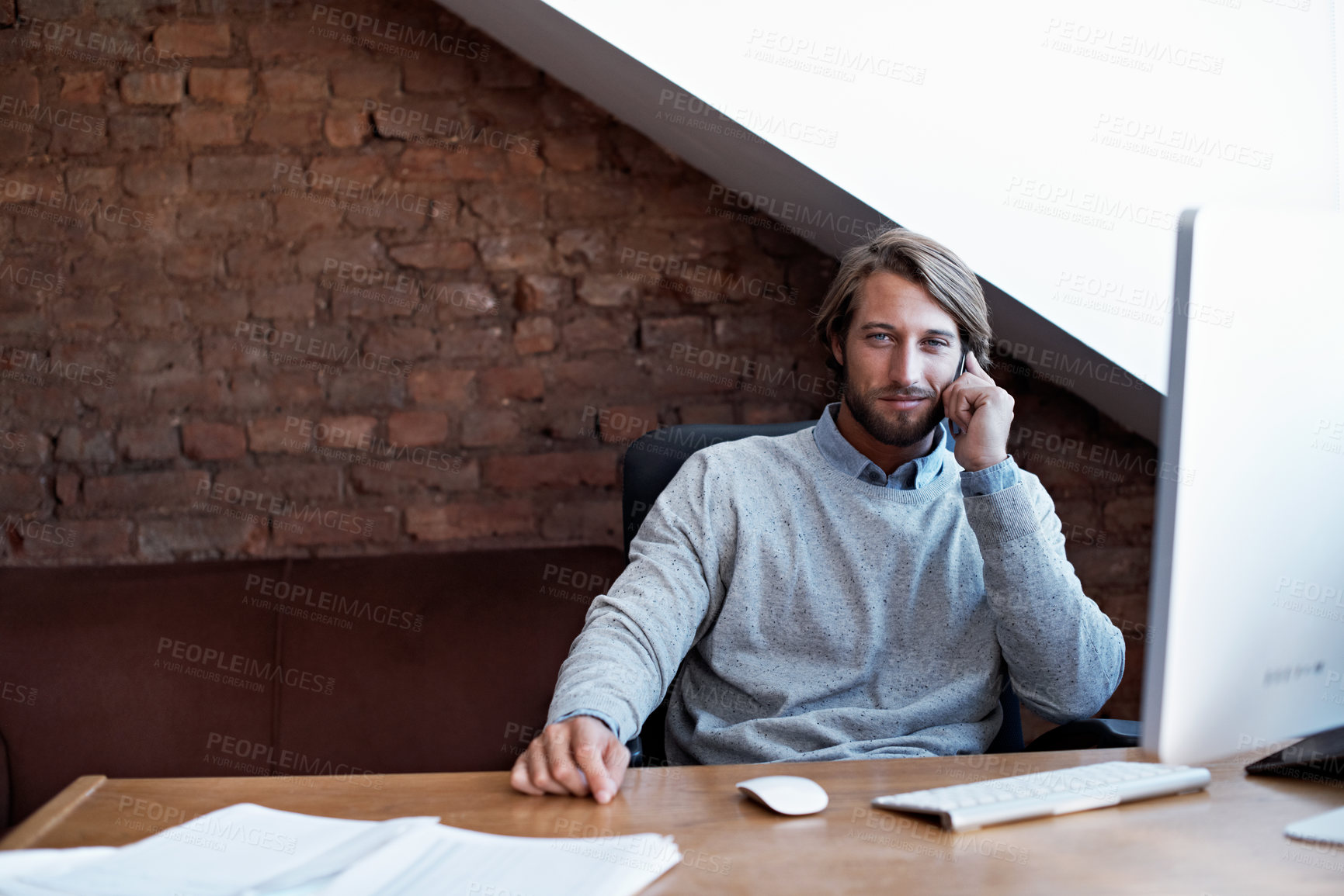 Buy stock photo Portrait of a young man talking on the phone while working on a computer at home