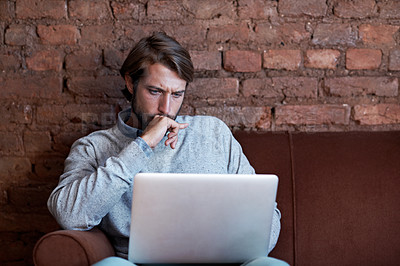 Buy stock photo Shot of a young man working on a laptop while sitting on a sofa at home