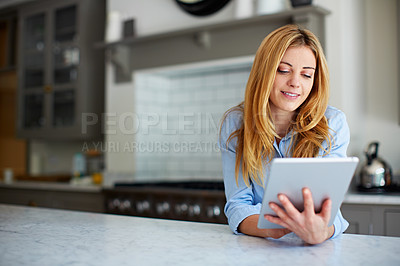 Buy stock photo Shot of a young woman leaning on her counter at home using a digital tablet