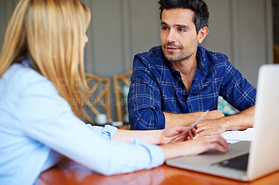 Buy stock photo Shot of a young couple sitting together at their kitchen table using a laptop