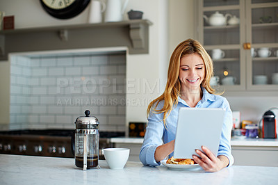 Buy stock photo Shot of a young woman leaning on her counter at home using a digital tablet and drinking coffee