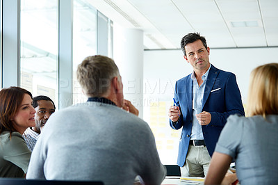 Buy stock photo Shot of a man giving a presentation to a group of colleagues sitting together in a modern office