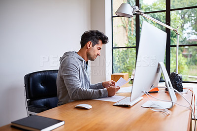 Buy stock photo Shot of a young man sorting paperwork while sitting at a desk in his home office