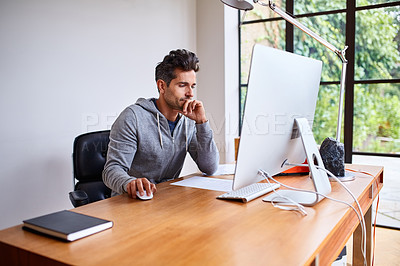Buy stock photo Shot of a young man working on a computer while sitting at a desk in his home office