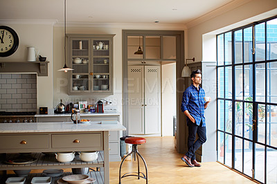 Buy stock photo Shot of a young man drinking coffee while looking out his kitchen window