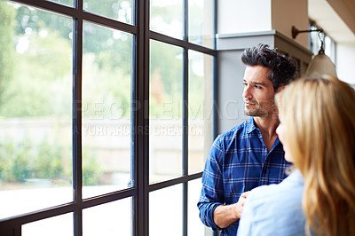 Buy stock photo Shot of a young couple looking out of a window together at home
