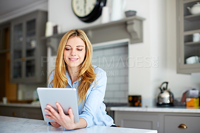 Buy stock photo Shot of a young woman leaning on her kitchen counter using a digital tablet