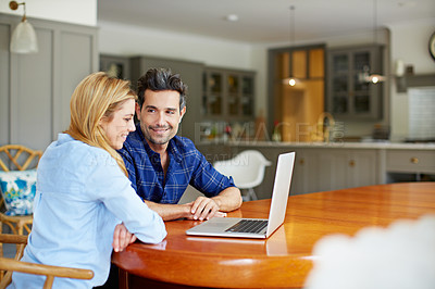 Buy stock photo Shot of a young couple sitting together at their kitchen table using a laptop