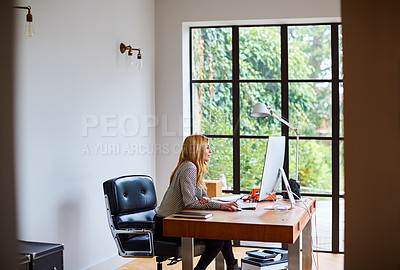 Buy stock photo Shot of a young woman working on a computer while sitting at a desk in her home office