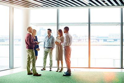 Buy stock photo Shot of a group of colleagues talking together while standing in an office hallway