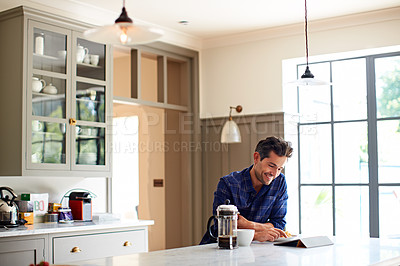 Buy stock photo Shot of a young man having breakfast and using a digital tablet in his kitchen