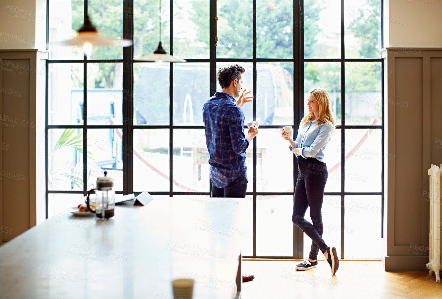 Buy stock photo Shot of a young couple drinking coffee together by a window in their kitchen