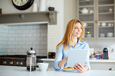 Buy stock photo Shot of a young woman leaning on her kitchen counter using a digital tablet