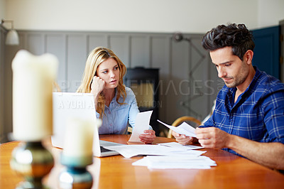 Buy stock photo Shot of a concerned looking young couple sitting together at their kitchen table paying bills online