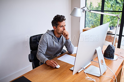Buy stock photo Shot of a young man working on a computer while sitting at a desk in his home office