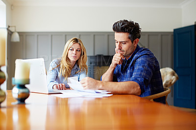 Buy stock photo Shot of a concerned looking young couple sitting together at their kitchen table paying bills online