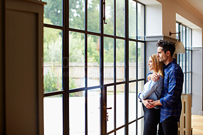 Buy stock photo Shot of a young couple looking out the window t home