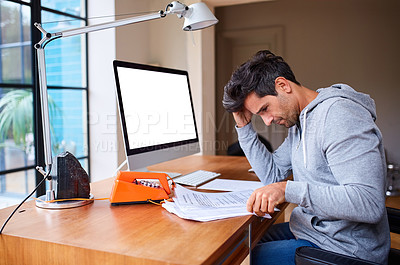 Buy stock photo Shot of a young man going through paperwork while working from home