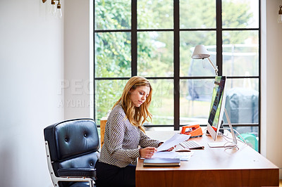 Buy stock photo Shot of a young woman going through paperwork while working from home