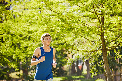 Buy stock photo Cropped shot of a handsome and athletic young sportsman listening to music while out for a jog in the park