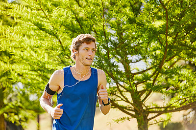 Buy stock photo Cropped shot of a handsome and athletic young sportsman listening to music while out for a jog in the park