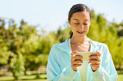 Buy stock photo Cropped shot of an attractive and athletic young sportswoman sending a text while out for a jog in the park