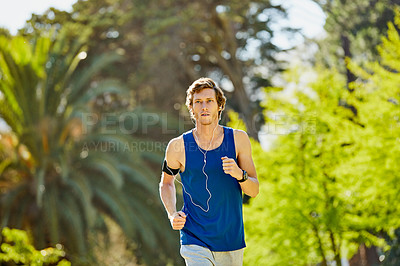 Buy stock photo Cropped shot of a handsome and athletic young sportsman listening to music while out for a jog in the park