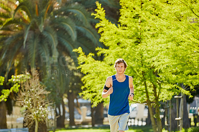 Buy stock photo Cropped shot of a handsome and athletic young sportsman listening to music while out for a jog in the park
