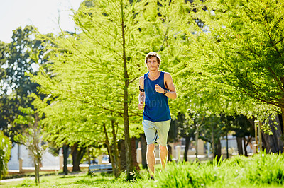 Buy stock photo Full length shot of a handsome and athletic young sportsman listening to music while out for a jog in the park