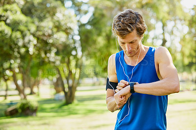 Buy stock photo Cropped shot of a handsome and athletic young sportsman checking his watch while out for a jog in the park