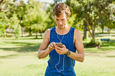 Buy stock photo Cropped shot of a handsome and athletic young sportsman sending a text while out for a jog in the park