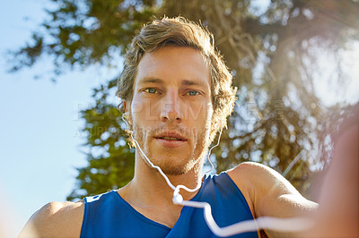 Buy stock photo Cropped portrait of a handsome and athletic young sportsman listening to music while out for a jog in the park